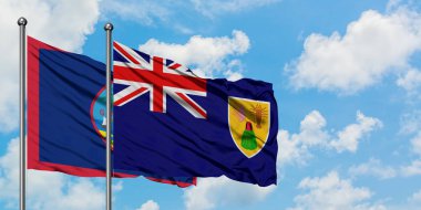 Guam ve Turks ve Caicos Adaları bayrağı birlikte beyaz bulutlu mavi gökyüzüne karşı rüzgarsal sallayarak. Diplomasi kavramı, uluslararası ilişkiler.