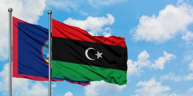 Guam ve Libya bayrağı birlikte beyaz bulutlu mavi gökyüzüne karşı rüzgarda sallayarak. Diplomasi kavramı, uluslararası ilişkiler.