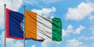 Guam ve Fildişi Sahili bayrağı birlikte beyaz bulutlu mavi gökyüzüne karşı rüzgarda sallayarak. Diplomasi kavramı, uluslararası ilişkiler.