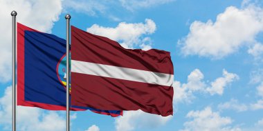 Guam ve Letonya bayrağı birlikte beyaz bulutlu mavi gökyüzüne karşı rüzgarda sallayarak. Diplomasi kavramı, uluslararası ilişkiler.