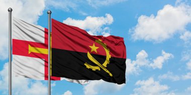 Guernsey ve Angola bayrağı birlikte beyaz bulutlu mavi gökyüzüne karşı rüzgarda sallayarak. Diplomasi kavramı, uluslararası ilişkiler.