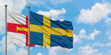 Guernsey ve İsveç bayrağı birlikte beyaz bulutlu mavi gökyüzüne karşı rüzgarda sallayarak. Diplomasi kavramı, uluslararası ilişkiler.