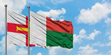 Guernsey ve Madagaskar bayrağı birlikte beyaz bulutlu mavi gökyüzüne karşı rüzgarda sallayarak. Diplomasi kavramı, uluslararası ilişkiler.