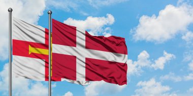 Guernsey ve Danimarka bayrağı birlikte beyaz bulutlu mavi gökyüzüne karşı rüzgarda sallayarak. Diplomasi kavramı, uluslararası ilişkiler.