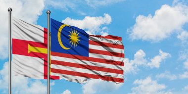 Guernsey ve Malezya bayrağı birlikte beyaz bulutlu mavi gökyüzüne karşı rüzgarda sallayarak. Diplomasi kavramı, uluslararası ilişkiler.