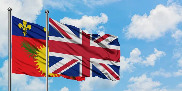 Guadalupe y la bandera del Reino Unido ondeando en el viento contra el cielo azul nublado blanco juntos. Concepto diplomático, relaciones internacionales . — Foto de Stock