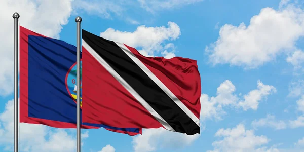 Guam e a bandeira de Trinidad e Tobago agitando no vento contra o céu azul nublado branco juntos. Conceito de diplomacia, relações internacionais . — Fotografia de Stock
