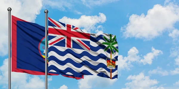 Guam y la bandera británica del Territorio del Océano Índico ondeando en el viento contra el cielo azul nublado blanco juntos. Concepto diplomático, relaciones internacionales . — Foto de Stock