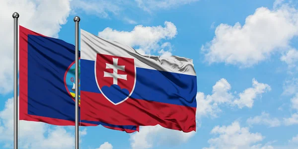 Bandera de Guam y Eslovaquia ondeando en el viento contra el cielo azul nublado blanco juntos. Concepto diplomático, relaciones internacionales . — Foto de Stock