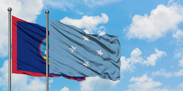 Bandera de Guam y Micronesia ondeando en el viento contra el cielo azul nublado blanco juntos. Concepto diplomático, relaciones internacionales . — Foto de Stock