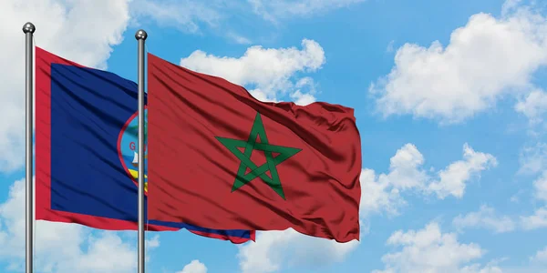 Bandera de Guam y Marruecos ondeando en el viento contra el cielo azul nublado blanco juntos. Concepto diplomático, relaciones internacionales . — Foto de Stock