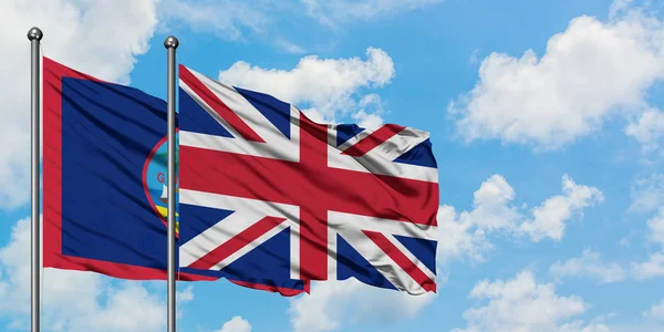 Guam y la bandera del Reino Unido ondeando en el viento contra el cielo azul nublado blanco juntos. Concepto diplomático, relaciones internacionales . — Foto de Stock