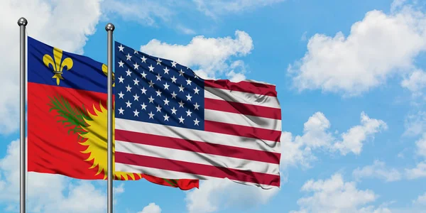 Guadalupe y la bandera de los Estados Unidos ondeando en el viento contra el cielo azul nublado blanco juntos. Concepto diplomático, relaciones internacionales . — Foto de Stock