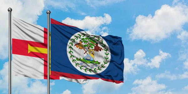 Bandera de Guernsey y Belice ondeando en el viento contra el cielo azul nublado blanco juntos. Concepto diplomático, relaciones internacionales . — Foto de Stock