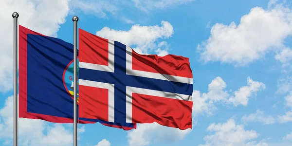 Bandera de Guam y Bouvet Islands ondeando en el viento contra el cielo azul nublado blanco juntos. Concepto diplomático, relaciones internacionales . — Foto de Stock