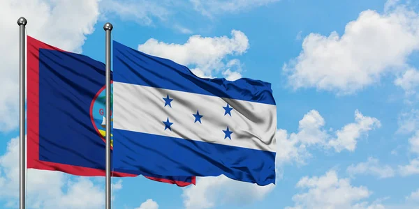 Η σημαία του Γκουάμ και της Ονδούρας κουνώντας τον άνεμο εναντίον του λευκού νεφελώδη μπλε ουρανού μαζί. Φιλοσοφία της διπλωματίας, διεθνείς σχέσεις. — Φωτογραφία Αρχείου