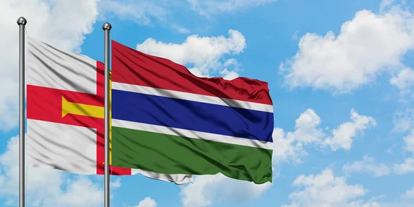 Guernsey e Gambia sventolano nel vento contro il bianco cielo blu nuvoloso insieme. Concetto di diplomazia, relazioni internazionali . — Foto Stock