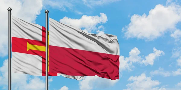 Guernsey a polská vlajka mávali ve větru proti bíle zatažené modré obloze. Diplomacie, mezinárodní vztahy. — Stock fotografie