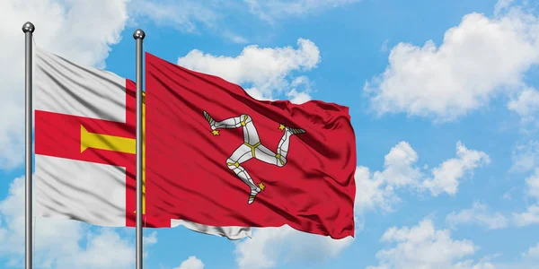 Guernsey y la bandera de la Isla de Man ondeando en el viento contra el cielo azul nublado blanco juntos. Concepto diplomático, relaciones internacionales . — Foto de Stock