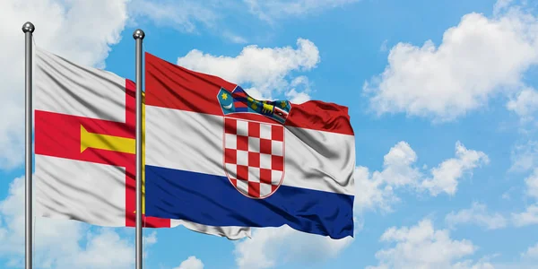 Bandera de Guernsey y Croacia ondeando en el viento contra el cielo azul nublado blanco juntos. Concepto diplomático, relaciones internacionales . — Foto de Stock