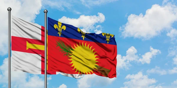 Bandera de Guernsey y Guadalupe ondeando en el viento contra el cielo azul nublado blanco juntos. Concepto diplomático, relaciones internacionales . — Foto de Stock