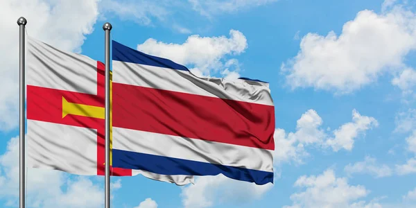 Guernsey e la bandiera del Costa Rica sventolano insieme nel vento contro il bianco cielo blu nuvoloso. Concetto di diplomazia, relazioni internazionali . — Foto Stock