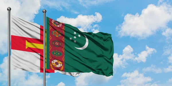 Bandera de Guernsey y Turkmenistán ondeando en el viento contra el cielo azul nublado blanco juntos. Concepto diplomático, relaciones internacionales . — Foto de Stock
