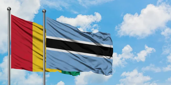 Guinejská a Botswanská vlajka mával ve větru proti bíle zatažené modré obloze. Diplomacie, mezinárodní vztahy. — Stock fotografie