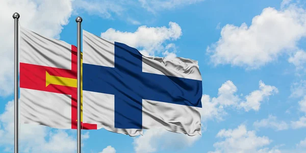 格恩西岛和芬兰国旗在风中飘扬，与白云相间的蓝天相一起。外交概念、国际关系. — 图库照片