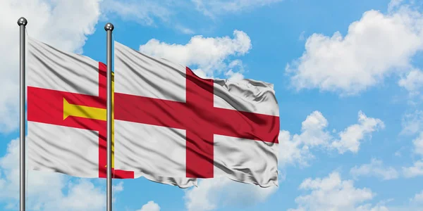 Bandera de Guernsey e Inglaterra ondeando en el viento contra el cielo azul nublado blanco juntos. Concepto diplomático, relaciones internacionales . — Foto de Stock