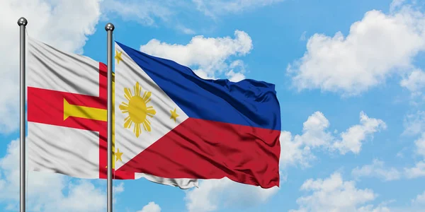 Bandera de Guernsey y Filipinas ondeando en el viento contra el cielo azul nublado blanco juntos. Concepto diplomático, relaciones internacionales . — Foto de Stock