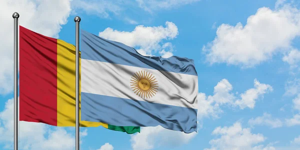 Bandera de Guinea y Argentina ondeando en el viento contra el cielo azul nublado blanco juntos. Concepto diplomático, relaciones internacionales . — Foto de Stock