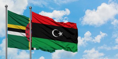 Dominika ve Libya bayrağı birlikte beyaz bulutlu mavi gökyüzüne karşı rüzgarda sallayarak. Diplomasi kavramı, uluslararası ilişkiler.