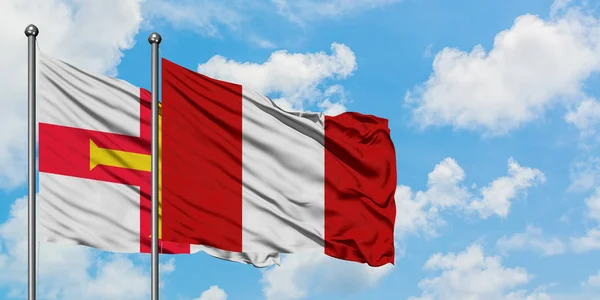 Bandera de Guernsey y Perú ondeando en el viento contra el cielo azul nublado blanco juntos. Concepto diplomático, relaciones internacionales . — Foto de Stock
