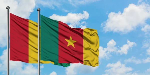Bandera de Guinea y Camerún ondeando en el viento contra el cielo azul nublado blanco juntos. Concepto diplomático, relaciones internacionales . — Foto de Stock