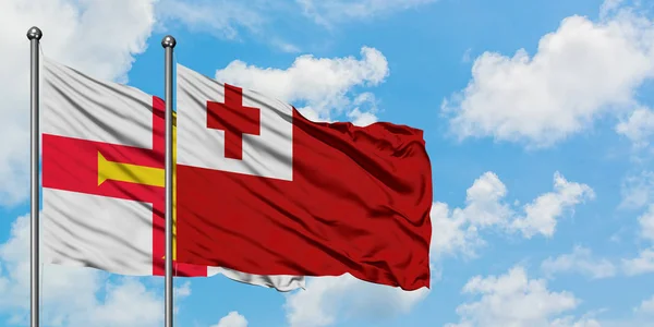 Guernsey a Tonga praporce mávali ve větru proti bíle zatažené modré obloze. Diplomacie, mezinárodní vztahy. — Stock fotografie