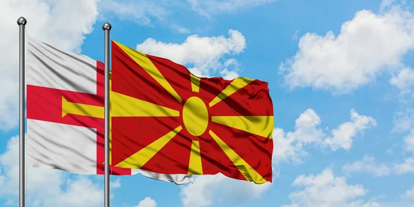 Guernsey en Macedonië vlag zwaaien in de wind tegen witte bewolkte blauwe hemel samen. Diplomatie concept, internationale betrekkingen. — Stockfoto