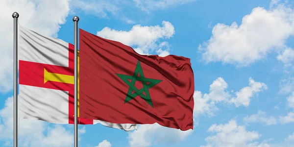 Bandera de Guernsey y Marruecos ondeando en el viento contra el cielo azul nublado blanco juntos. Concepto diplomático, relaciones internacionales . — Foto de Stock