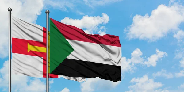 Bandera de Guernsey y Sudán ondeando en el viento contra el cielo azul nublado blanco juntos. Concepto diplomático, relaciones internacionales . — Foto de Stock