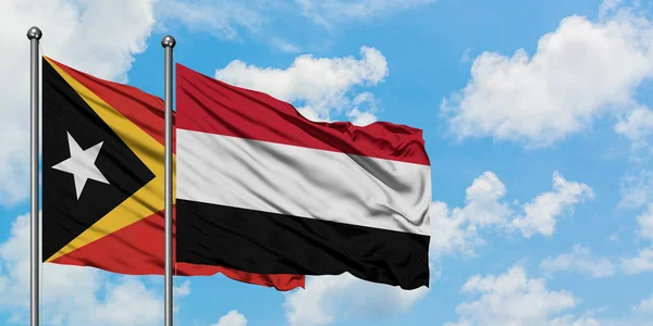 Timor Oriental y la bandera de Yemen ondeando en el viento contra el cielo azul nublado blanco juntos. Concepto diplomático, relaciones internacionales . — Foto de Stock