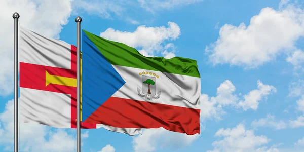 Bandera de Guernsey y Guinea Ecuatorial ondeando en el viento contra el cielo azul nublado blanco juntos. Concepto diplomático, relaciones internacionales . — Foto de Stock