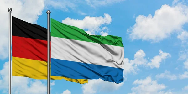 Bandera de Alemania y Sierra Leona ondeando en el viento contra el cielo azul nublado blanco juntos. Concepto diplomático, relaciones internacionales . — Foto de Stock