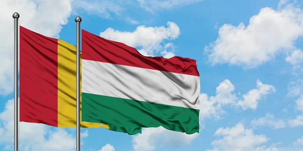 Bandera de Guinea y Hungría ondeando en el viento contra el cielo azul nublado blanco juntos. Concepto diplomático, relaciones internacionales . — Foto de Stock