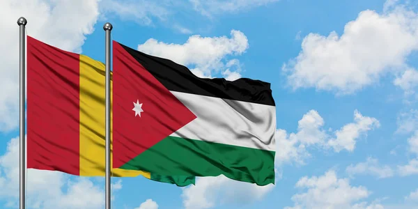Bandera de Guinea y Jordania ondeando en el viento contra el cielo azul nublado blanco juntos. Concepto diplomático, relaciones internacionales . — Foto de Stock