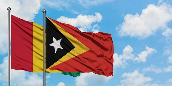 Bandera de Guinea y Timor Oriental ondeando en el viento contra el cielo azul nublado blanco juntos. Concepto diplomático, relaciones internacionales . — Foto de Stock