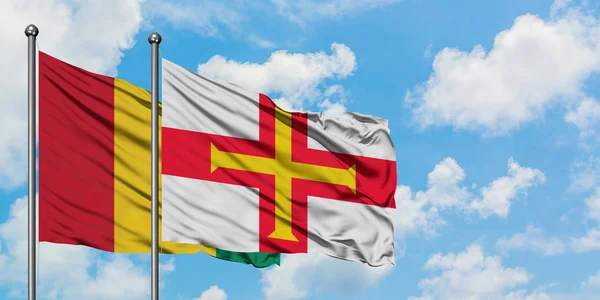 Guinea och Guernsey sjunker vinka i vinden mot vit grumlig blå himmel tillsammans. Diplomatisk koncept, internationella relationer. — Stockfoto