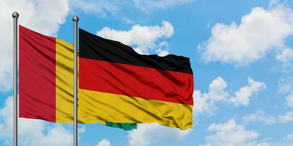 Bandera de Guinea y Alemania ondeando en el viento contra el cielo azul nublado blanco juntos. Concepto diplomático, relaciones internacionales . —  Fotos de Stock