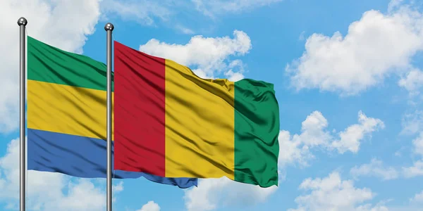 Drapeau du Gabon et de la Guinée agitant dans le vent contre ciel bleu nuageux blanc ensemble. Concept de diplomatie, relations internationales . — Photo