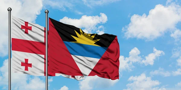 Gürcistan ve Antigua ve Barbuda bayrağı birlikte beyaz bulutlu mavi gökyüzüne karşı rüzgarda sallayarak. Diplomasi kavramı, uluslararası ilişkiler. — Stok fotoğraf