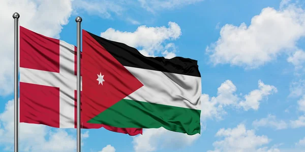 Bandera de Dinamarca y Jordania ondeando en el viento contra el cielo azul nublado blanco juntos. Concepto diplomático, relaciones internacionales . — Foto de Stock